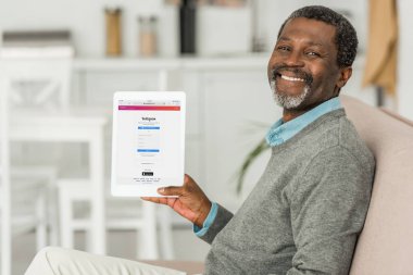 Kyiv, Ukrayna - 2 Ekim 2019: Instagram uygulamalı dijital tablet tutan ve kameraya gülümseyen neşeli Afrikalı Amerikalı adam.