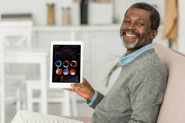 Neşeli Afro-Amerikan adam dijital tablet tutuyor ekranda bilgi ve kameraya gülümsüyor.