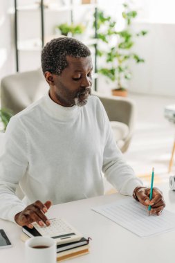 Masada oturan ve ortak harcamaları hesaplayan özenli Afro-Amerikan adam.