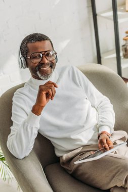 Elinde dijital tablet tutarken kulaklıkla müzik dinleyen şık Afro-Amerikan bir adam.