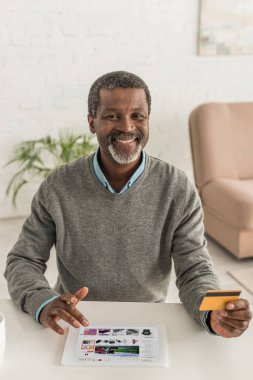 Kyiv, Ukrayna - 2 Ekim 2019: Neşeli Afrikalı Amerikalı adam kredi kartı tutuyor ve ekranda aliexpress uygulaması olan dijital tablet kullanıyor.