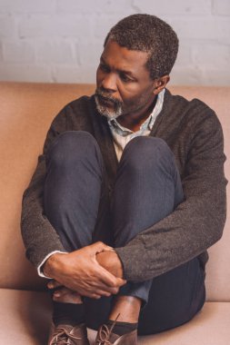 Bunalımlı Afro-Amerikan adam evdeki kanepede oturuyor ve başka tarafa bakıyor.