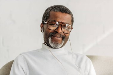 Şık, son sınıf Afro-Amerikalı gözlüklü adam kulaklıkla müzik dinliyor ve kameraya gülümsüyor.