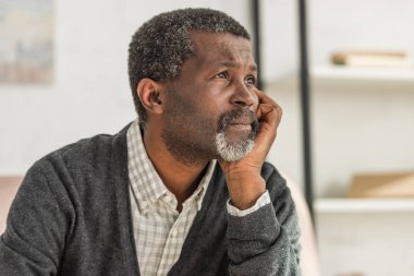 depressed, senior african american man holding hand near face and looking away clipart