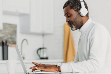 Kulaklıklı, dizüstü bilgisayarda yazan konsantre Afro-Amerikan bir adam.