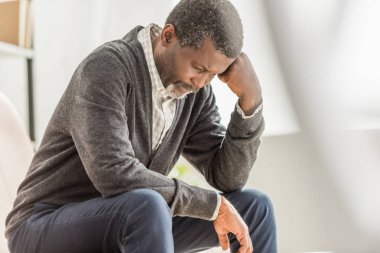 selective focus of depressed african american man sitting with bowed head clipart