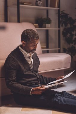 Afro-Amerikan adamın cesareti kırılmış yerde oturuyor ve faturaları tutuyor.