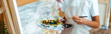 Gouache boyalı renkli palet tutan çocuğun panoramik görüntüsü. 