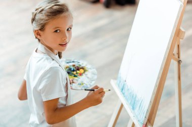 Sanat okulunda elinde rengarenk palet tutan sevimli bir çocuk.  