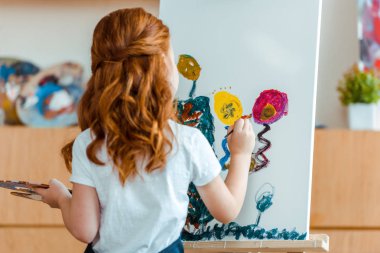 Sanat okulunda tuvale resim yapan kızıl saçlı çocuğun arka görünüşü 