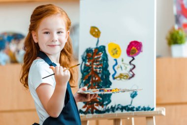 Sanat okulunda resim yaparken gülümseyen kızıl saçlı çocuk. 