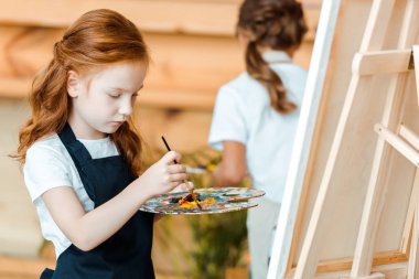 Sanat okulunda resim yapan sevimli kızıl saçlı çocuğun seçici odak noktası.
