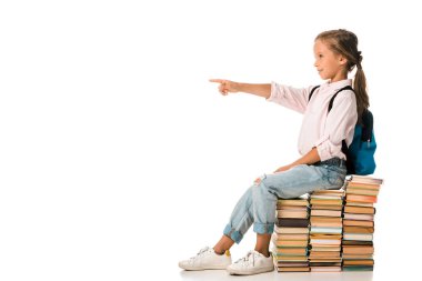 Neşeli çocuk kitapların üzerinde oturuyor ve parmağıyla beyazı işaret ediyor. 