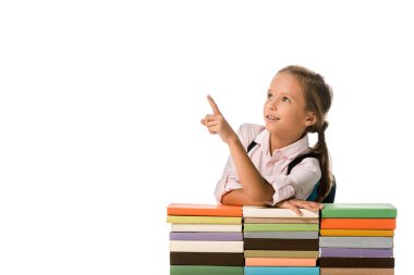 Pozitif okul çocuğu, beyaz üzerine izole edilmiş renkli kitaplara bakarken parmağıyla işaret ediyor. 
