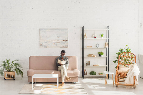 senior african american man reading book while sitting on sofa in living room