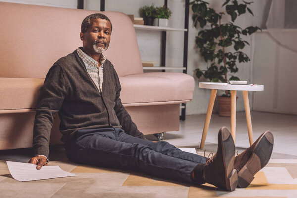 upset african american man sitting on floor and holding utility bill