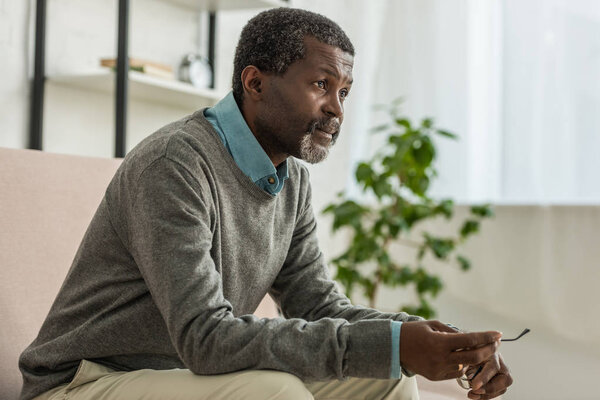 thoughtful african american man holding glasses and looking away