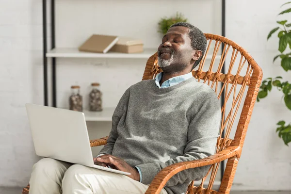 Hombre Afroamericano Mayor Sentado Silla Mimbre Sonriendo Utilizando Ordenador Portátil —  Fotos de Stock