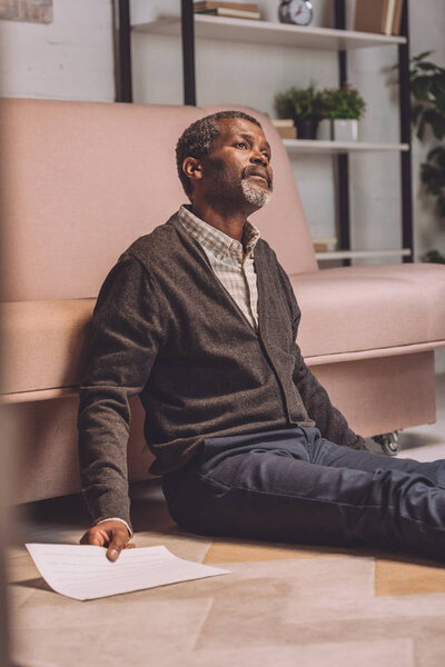 selective focus of upset african american man sitting on floor and holding utility bill