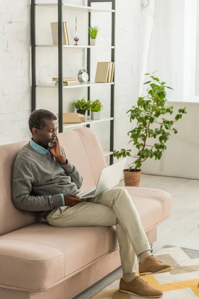 Pensativo Homem Americano Africano Sentado Sofá Sala Estar Usando Laptop — Fotografia de Stock