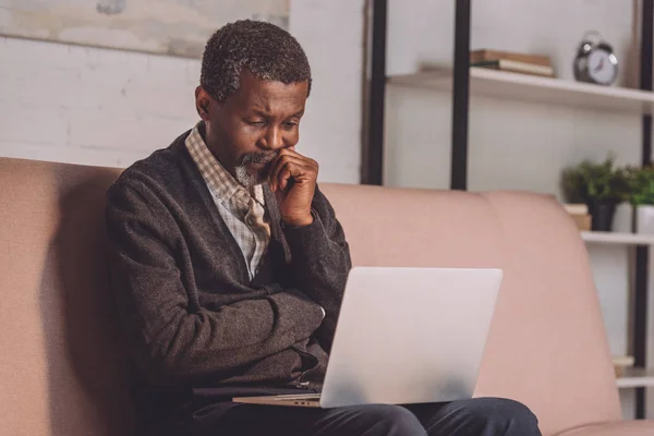 Chateado Afro Americano Homem Olhando Para Laptop Enquanto Sentado Sofá — Fotografia de Stock