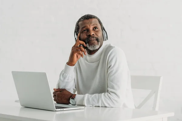 생각있는 아프리카 미국인 남자가 노트북 근처에 앉아서 보면서 헤드폰으로 음악을 — 스톡 사진