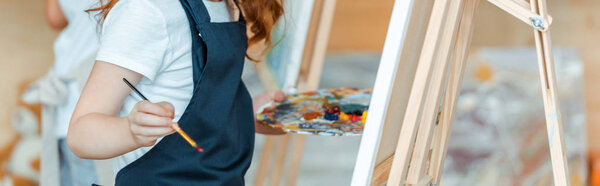 panoramic shot of child painting on canvas in art school 