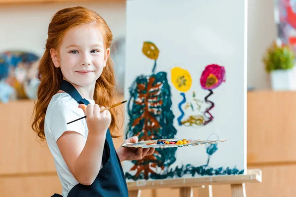 Sonriente Pelirroja Niño Pie Cerca Pintura Sobre Lienzo Escuela Arte — Foto de Stock