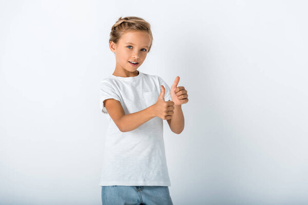 cheerful kid looking at camera and showing thumb up on white 