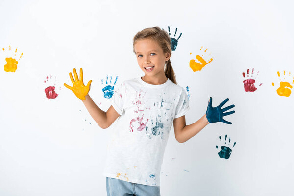 kid with blue and yellow paint on hands near hand prints on white 