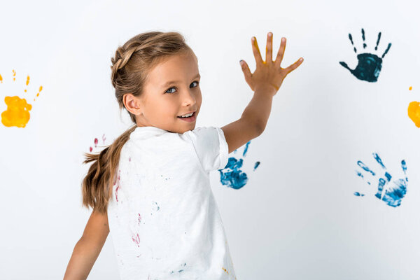 cheerful kid putting hand near hand prints on white 