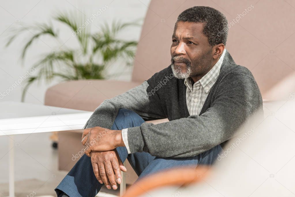 depressed african american man sitting on floor at home and looking away
