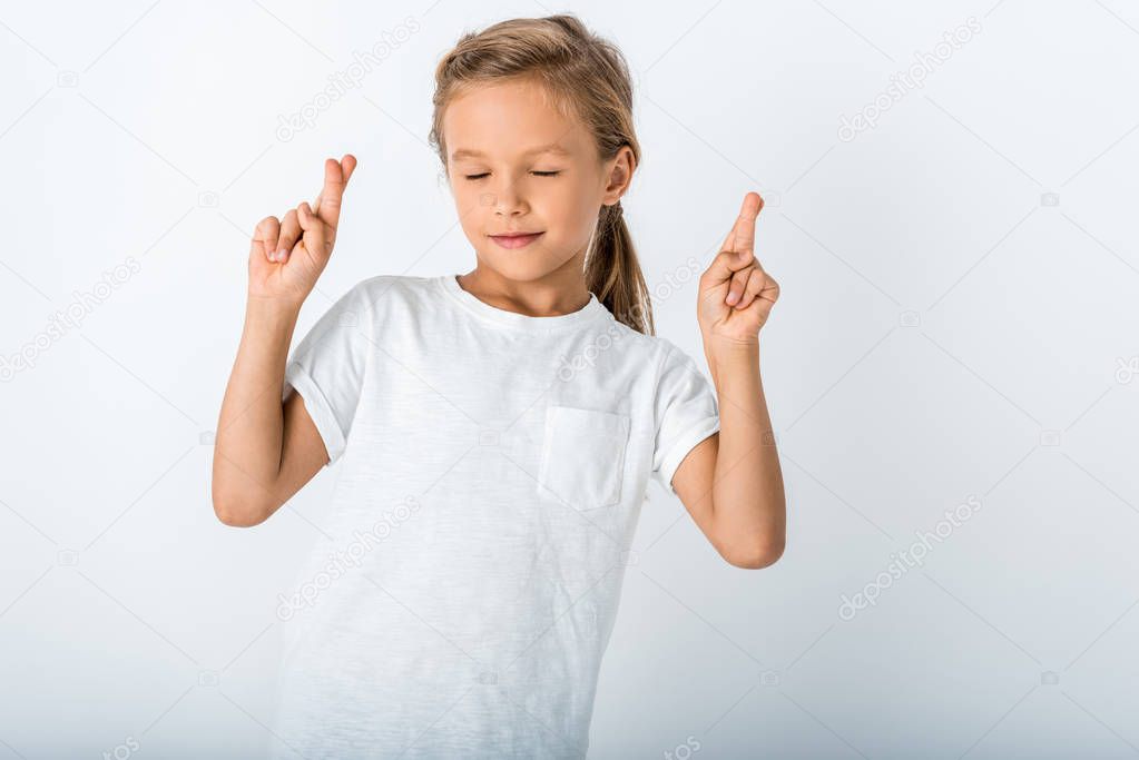 cute kid with closed eyes and fingers crossed on white 