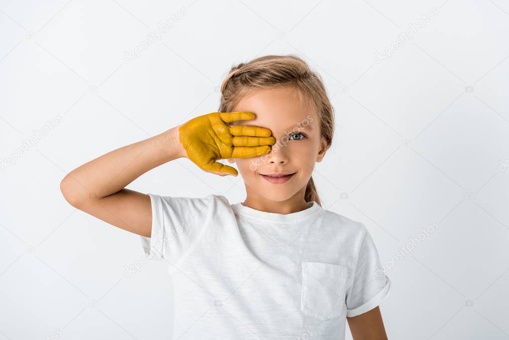 happy kid with yellow paint on hand covering face isolated on white 