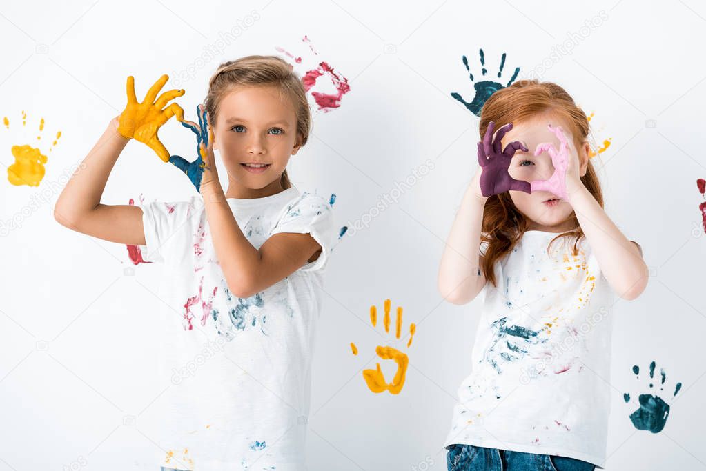 happy kids showing heart-shaped sign with hands in colorful paint on white 