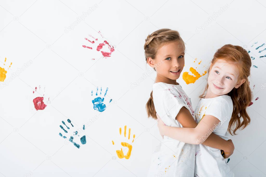 cheerful kids hugging near hand prints on white 