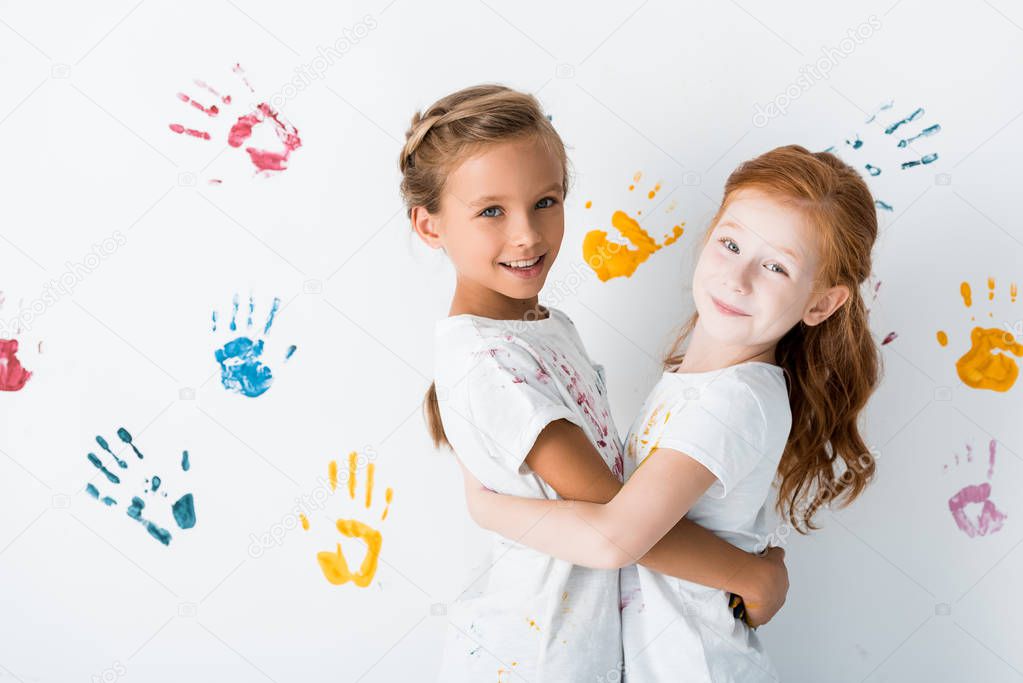 happy kids hugging near hand prints on white 