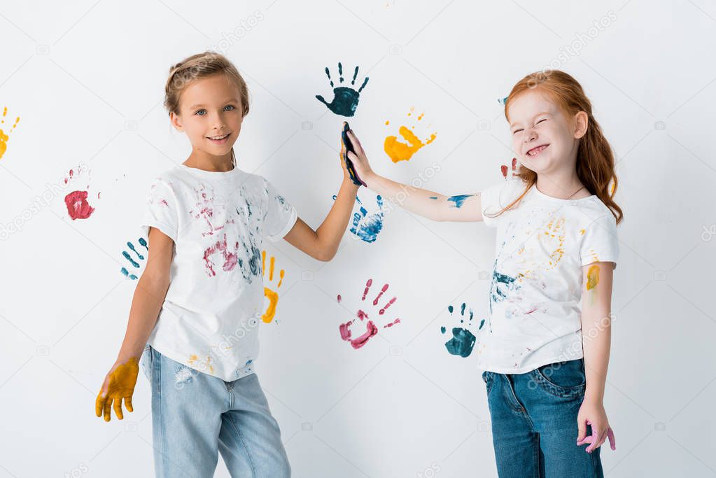 cheerful kids giving high five near hand prints on white 