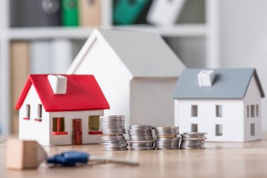 selective focus of stacked coins near house models and keys on wooden table clipart