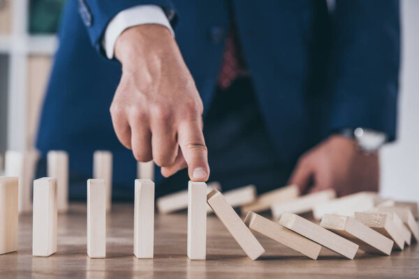 partial view of risk manager blocking domino effect of falling wooden blocks 