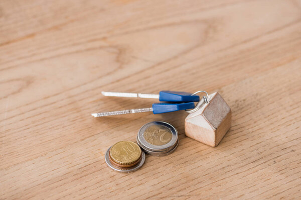 keys with toy house trinket near golden and silver coins on wooden table