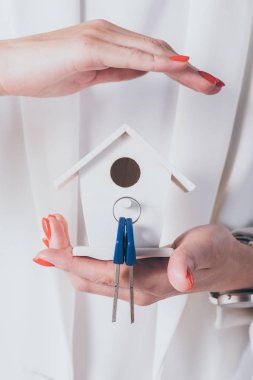 partial view of businesswoman holding and covering house model and keys with hand clipart