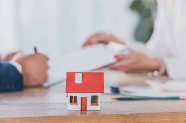 Pano tutan iş kadını yakınındaki ev modelinin seçici odak noktası ve sözleşme imzalayan müşteri