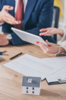 Dijital tablet tutan kadının yanındaki ev modelinin seçici odak noktası ve el ile işaret eden işadamı