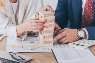 cropped view of risk managers sitting at workplace near stacked wooden blocks clipart