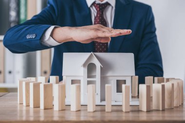 cropped view of risk manager covering house model surrounded with wooden blocks with hand
