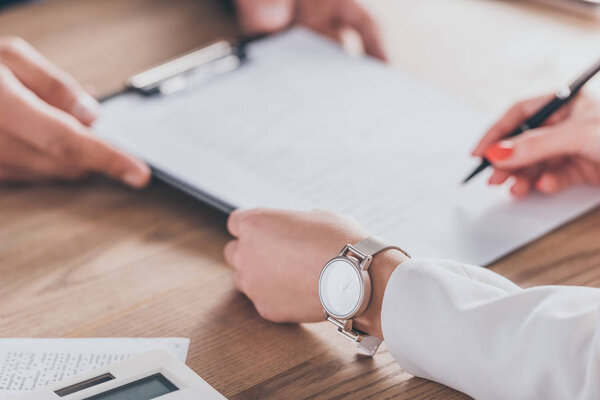 cropped view of woman in wristwatch signing contract near dealer