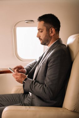 Sakallı iş adamının özel jette akıllı telefon kullanışının yan görüntüsü 