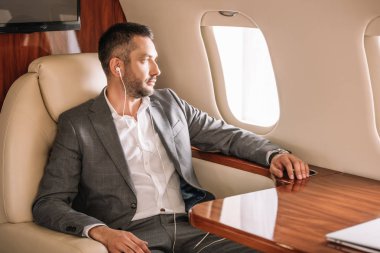 Müzik dinleyen ve uçak camına bakan yakışıklı iş adamlarının seçici odağı 