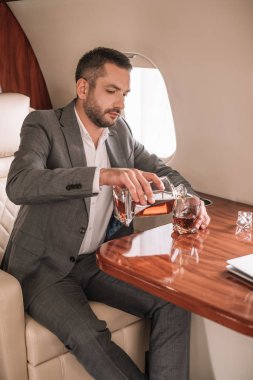 Yakışıklı işadamı özel jette otururken bardağa viski dolduruyor. 